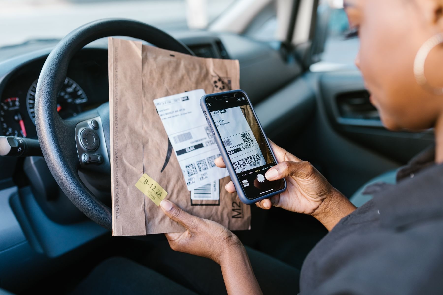 A courier scans a parcel label with her phone from the driver's seat
