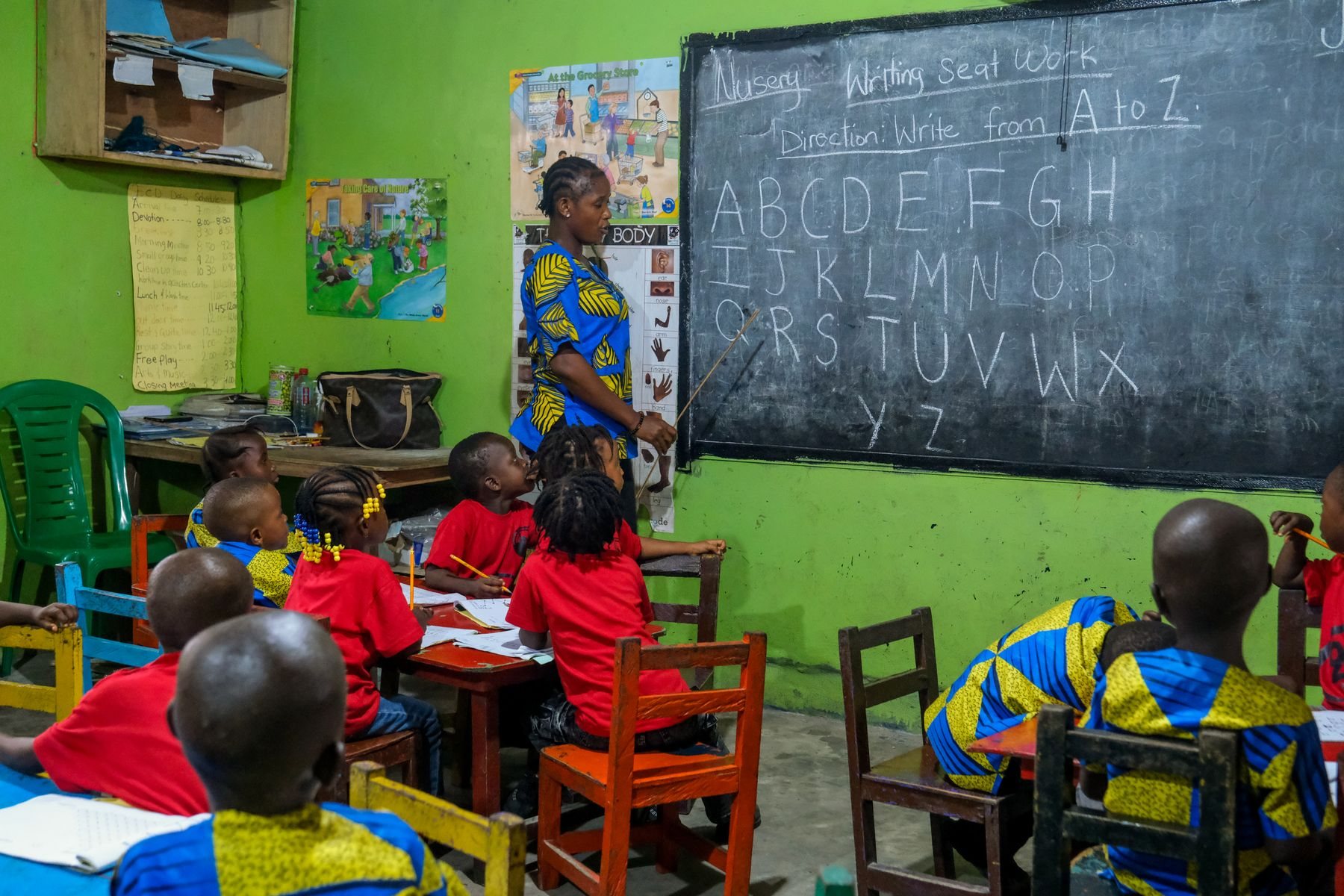 A teacher in blue ankara at the chalkboard with a class of young pupils