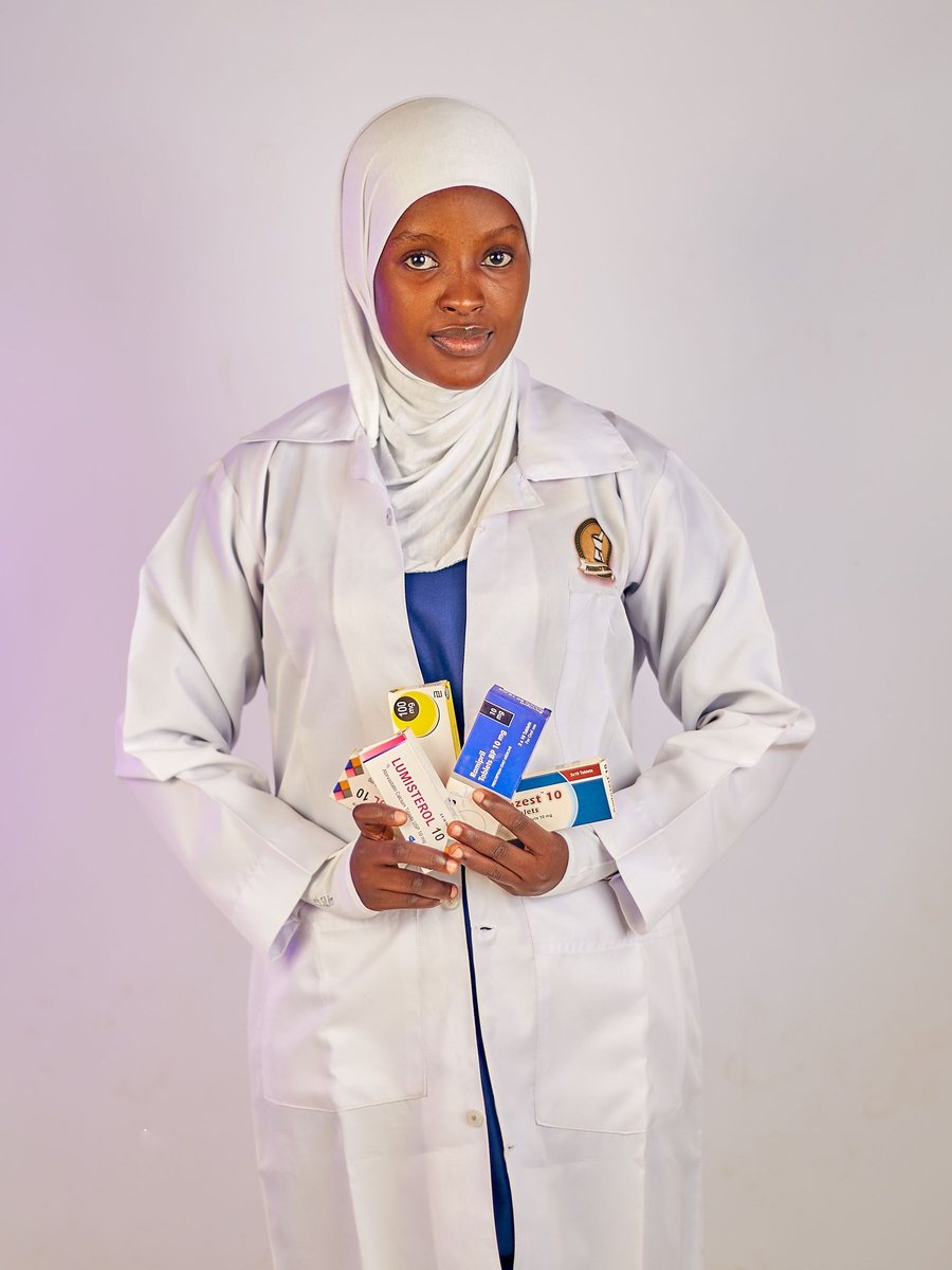 A pharmacist in a white coat and hijab holds boxes of medicine