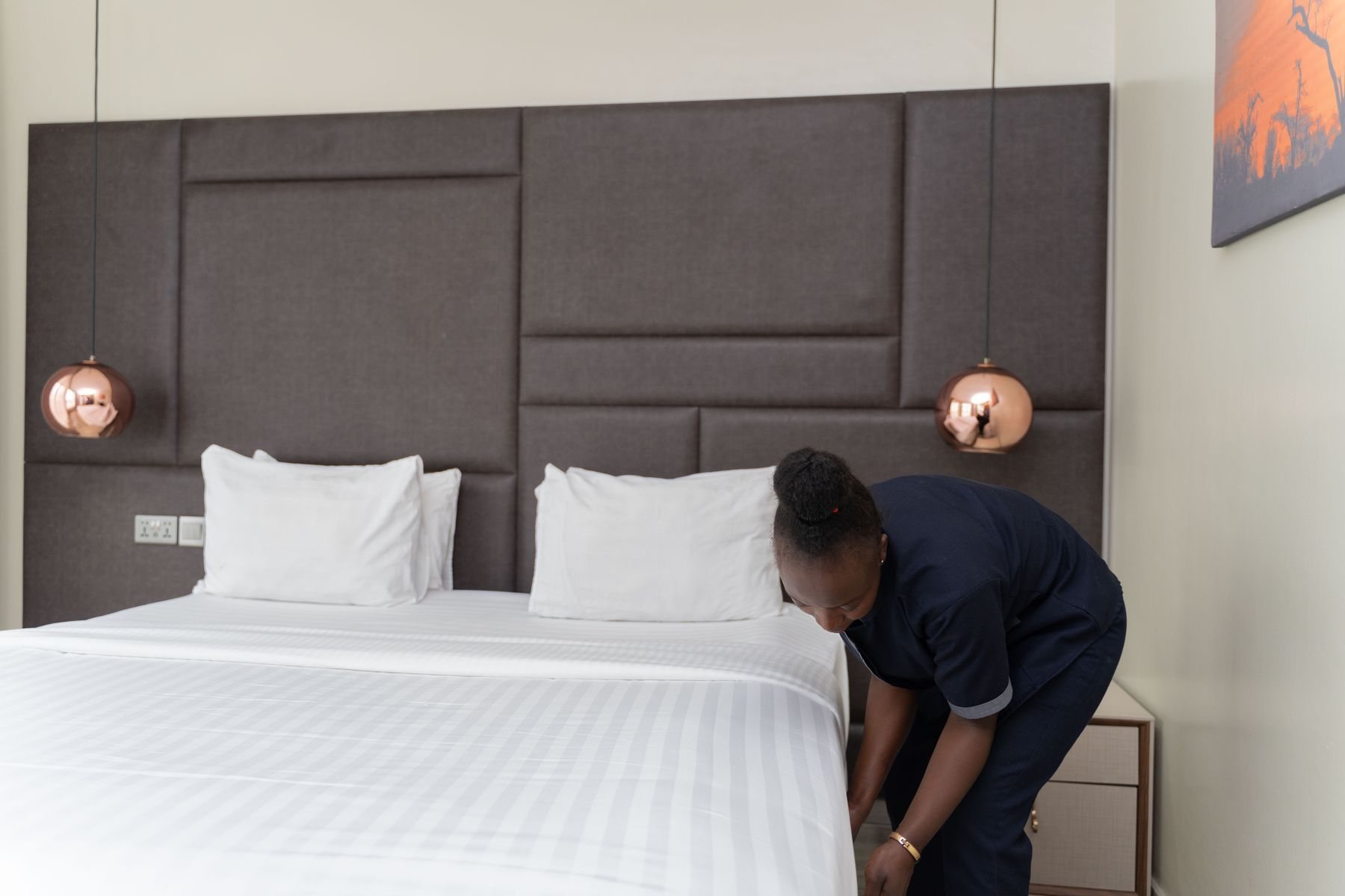 A housekeeper tucks crisp white linen on a king bed