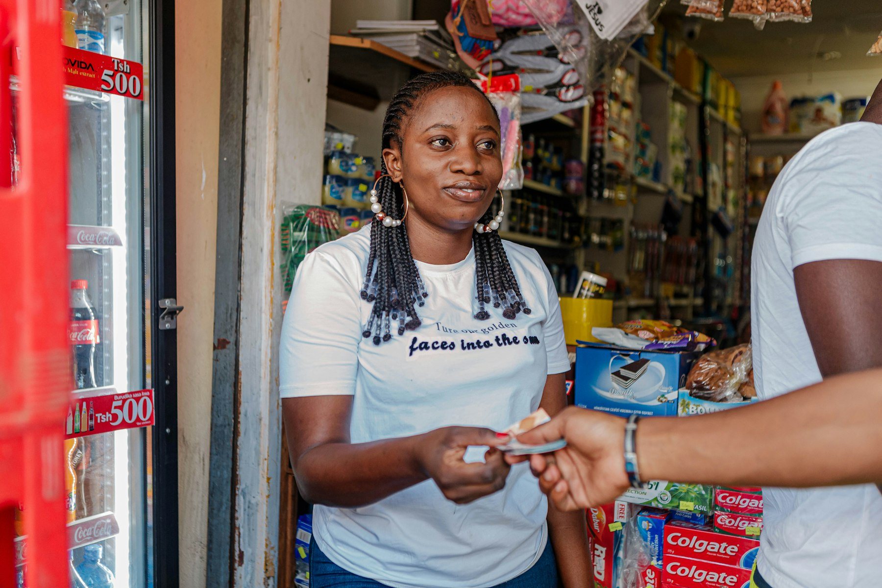 A kiosk owner smiles as she takes a payment at her shop counter